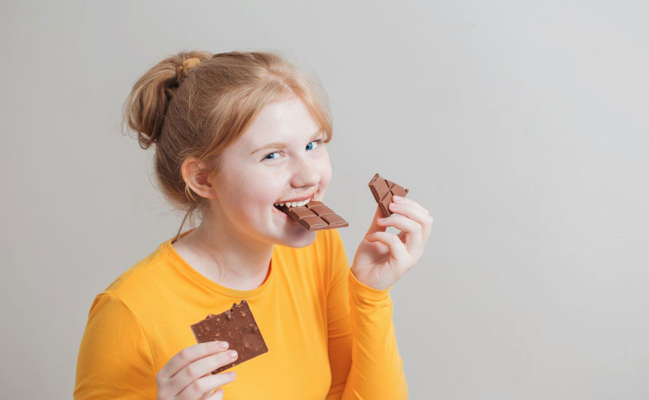 young girl eating chocolate with two hand and smilling